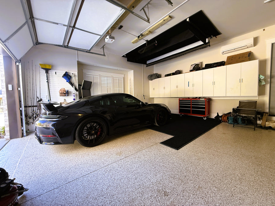 Garage with a retractable golf simultor and a black car parked inside, cabinets, and tools.