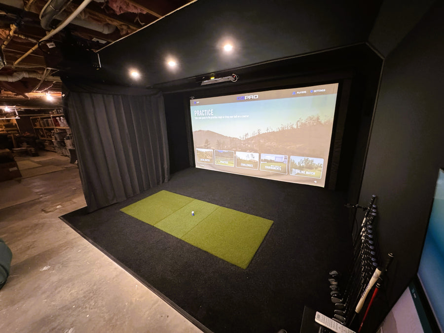 Golf simulator setup with screen displaying a golf course on a black wall.