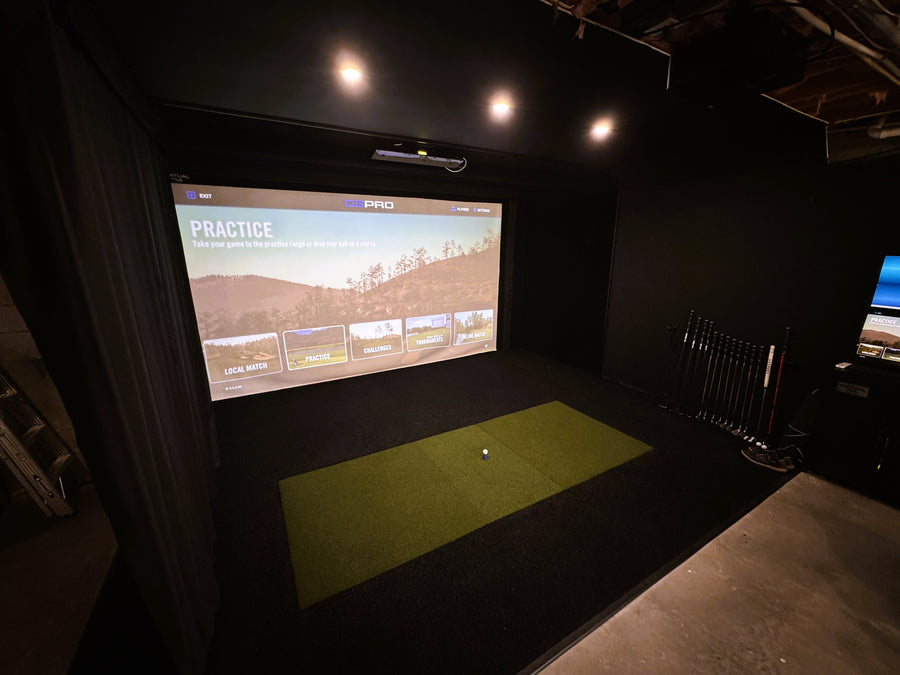 Indoor golf practice area with a screen displaying a golf course and a green mat on the floor.