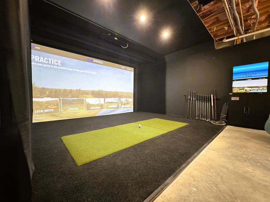 Indoor golf simulator setup with screen, mat, and golf clubs.