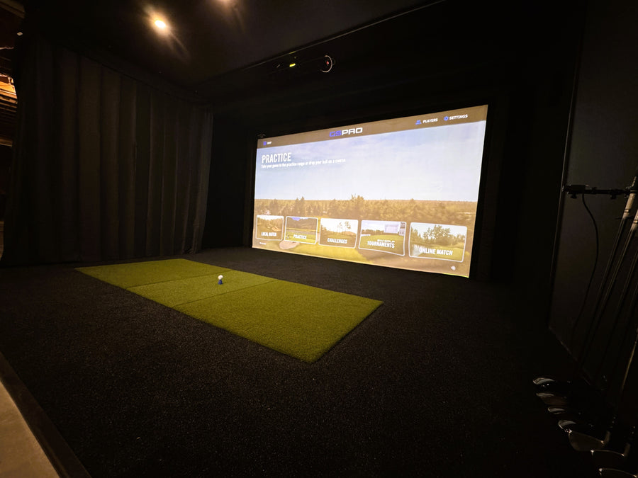 Golf simulator setup with screen displaying a golf course and a green mat on the floor.