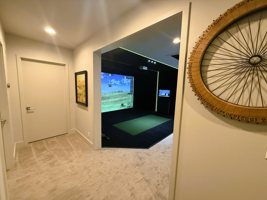 Golf simulator setup in a room with a large mirror reflecting the screen and wall decorations.