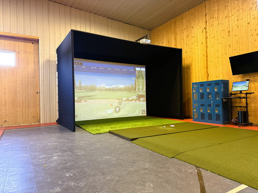 Indoor golf simulator setup with screen and green mat on wooden floor