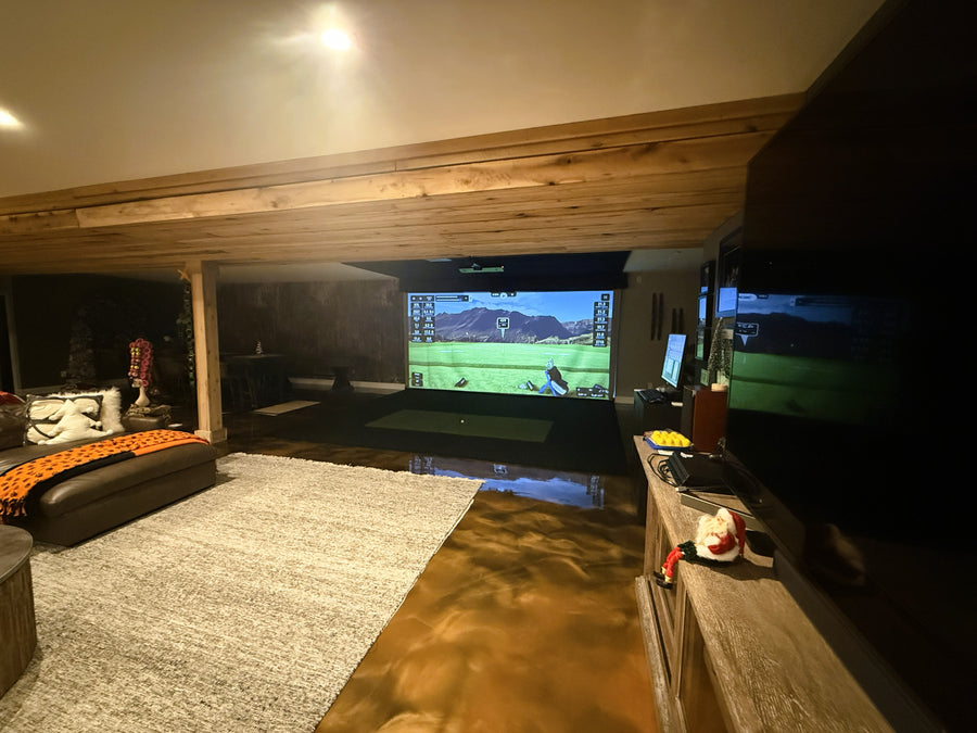 Indoor golf simulator setup with a large screen displaying a video game, surrounded by furniture and decor.