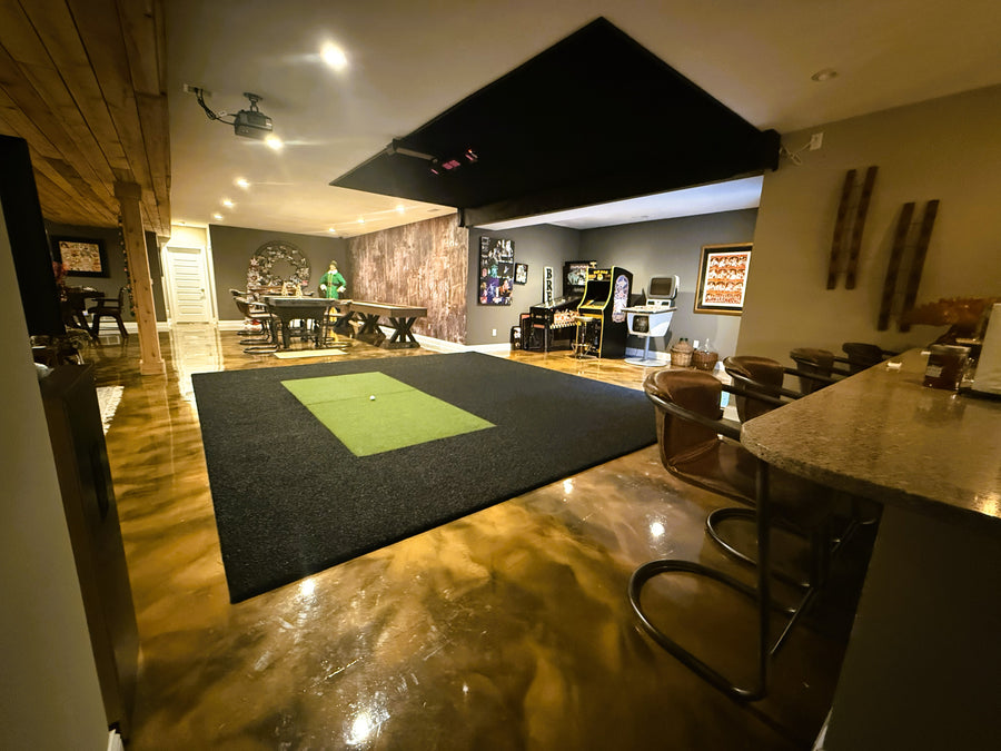 Indoor golf simulator setup with a putting green, bar stools, and a pool table.