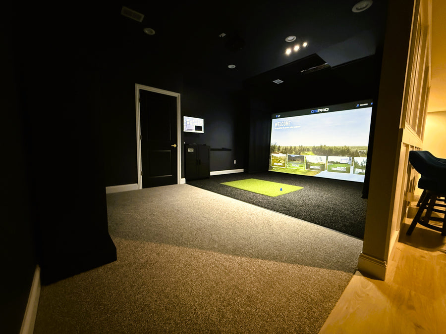 Indoor golf simulator setup in a dark room with a screen displaying a golf course.