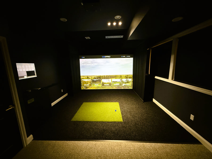 Dark room with a golf simulator, flanked by two smaller screens.