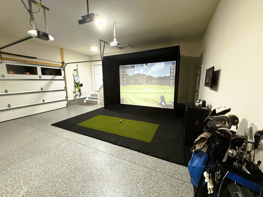 Indoor golf simulator setup in a garage with a screen displaying a golf course.