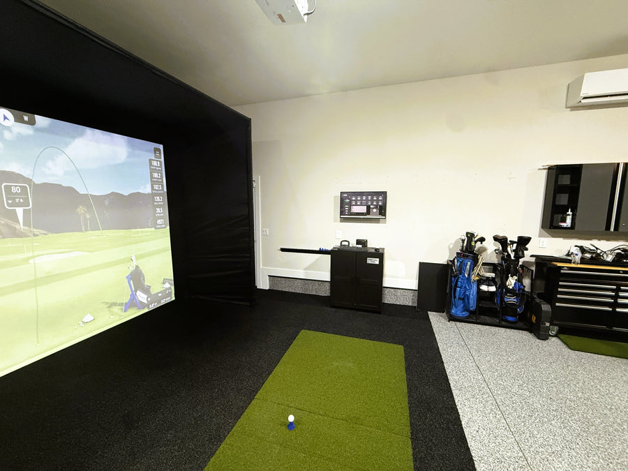 Golf simulator setup in a room with a screen displaying a golf game, surrounded by golf equipment.