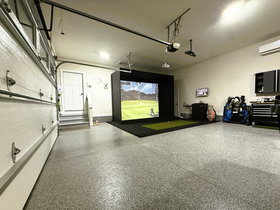 Garage with a golf simulator setup on a screen, surrounded by various equipment and furniture.