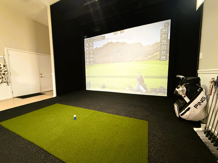Golf simulator setup with screen displaying a golf course, golf club, and ball on a green mat.