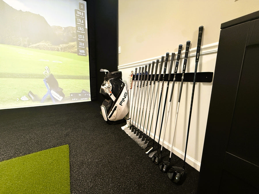 Golf simulator setup with golf clubs and bag on a wall-mounted rack.