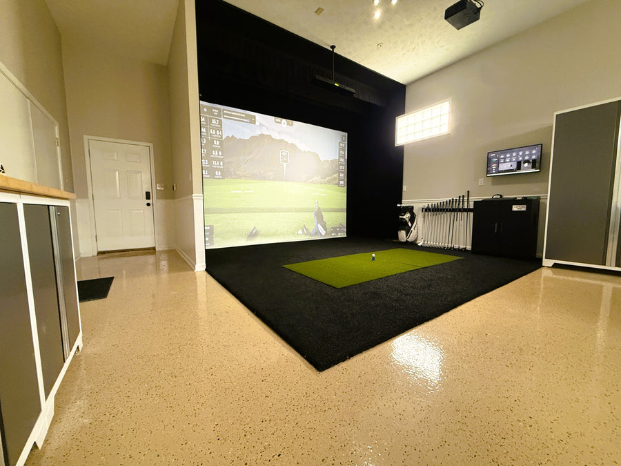 Indoor golf simulator room with screen displaying a golf course.