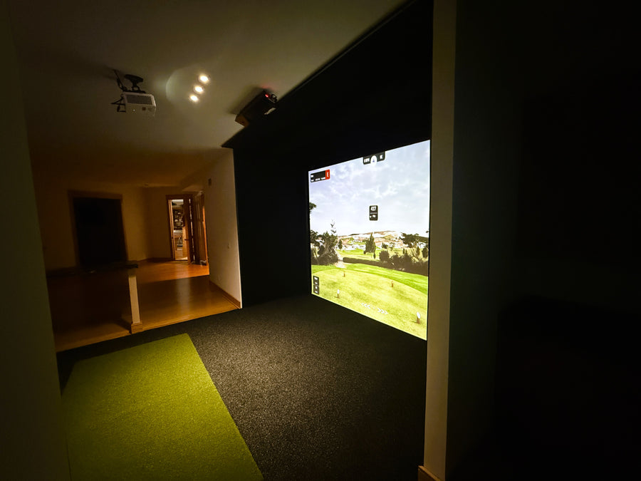 Indoor golf simulator setup with screen displaying a golf course.