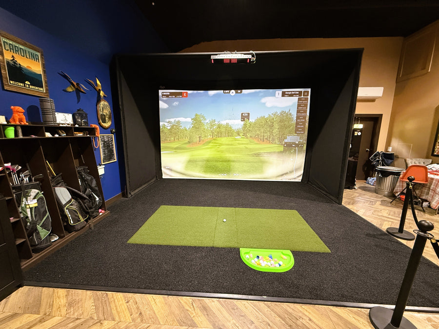 Golf simulator setup in a room with a screen displaying a golf course.