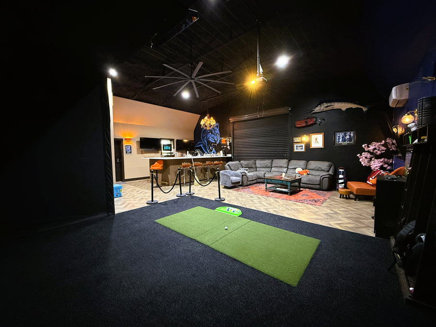 Indoor golf simulator area with a green mat, couch, and various decor items.