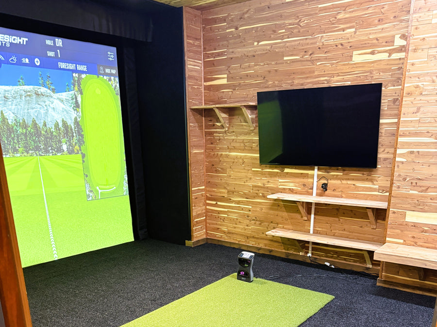 Golf simulator setup with screen and TV in a room with wooden walls and carpeted floor.