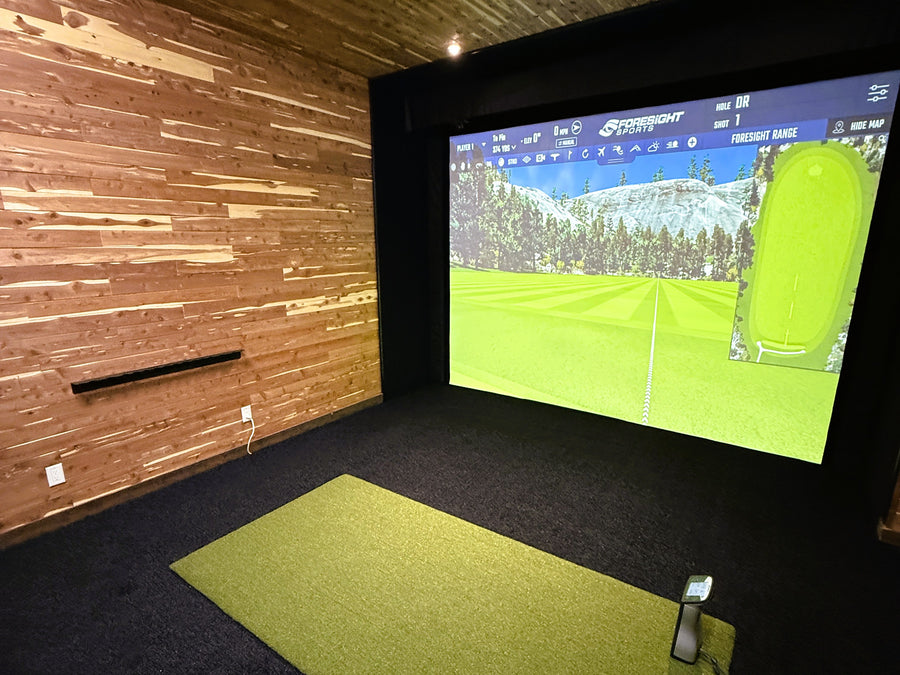 Indoor golf simulator setup with screen displaying a golf course and wooden wall.