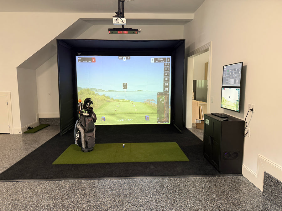 simple garage golf simulator setup with a golf bag, turf, and desk.