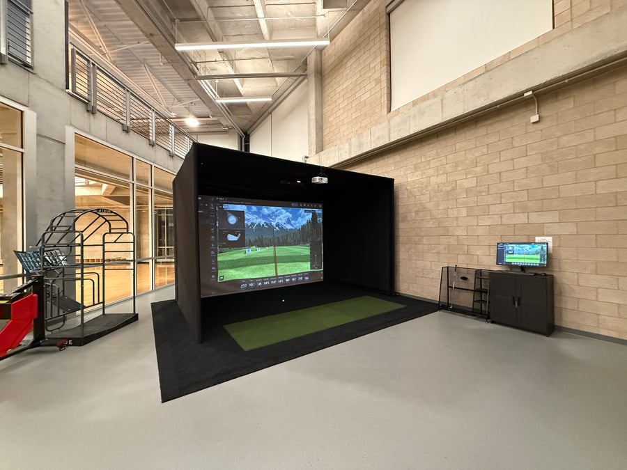 Golf simulator setup in a modern indoor facility with a screen displaying a golf course.