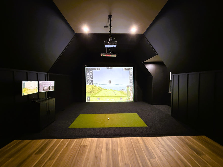 Indoor golf simulator setup with projection screen and green mat on wooden floor.