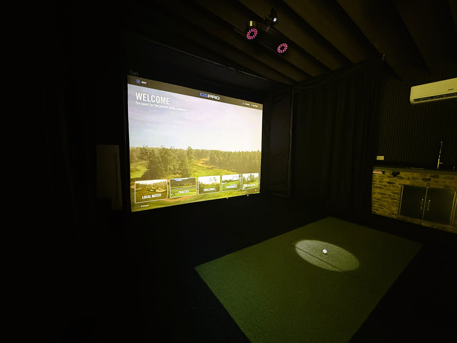 Golf simulator room with screen displaying a golf course and projected ball on the floor.