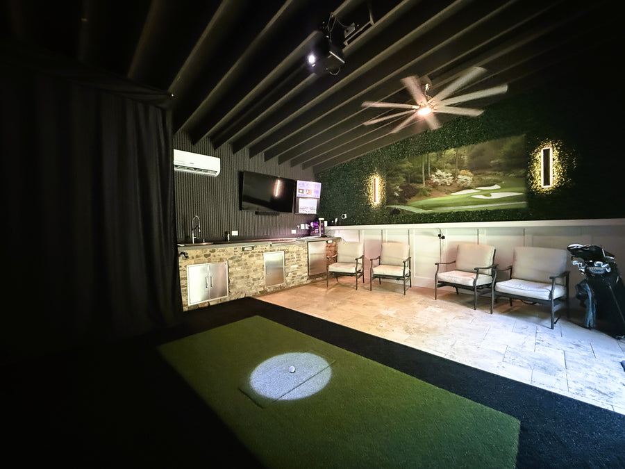 Indoor golf simulator with projection on the floor, surrounded by chairs and a bar area.