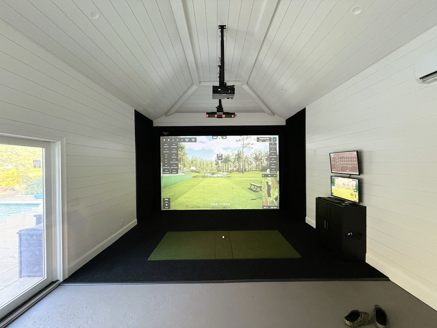Indoor golf simulator setup in a room with a screen displaying a golf course.