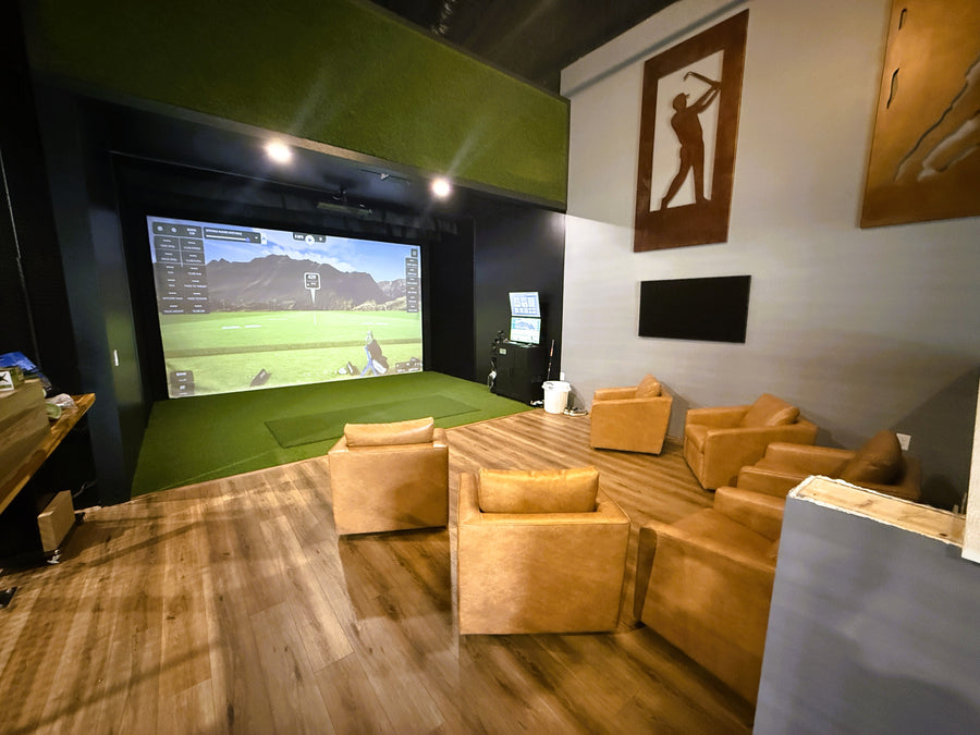 Golf Simulator room built with green turf around it and brown leather seating behind it.