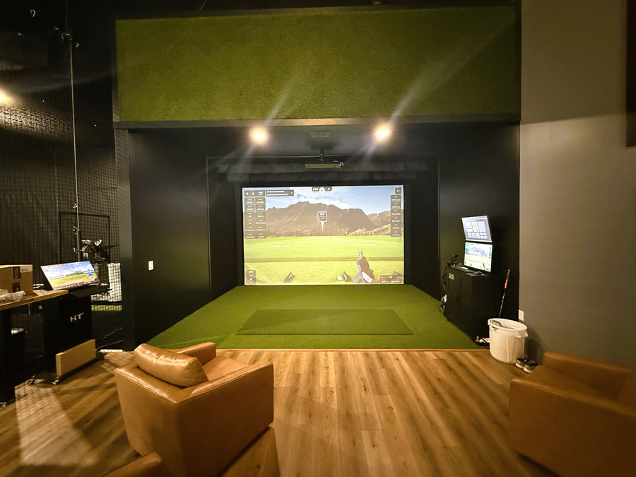 Golf Simulator room built with green turf around it and brown leather seating behind it.