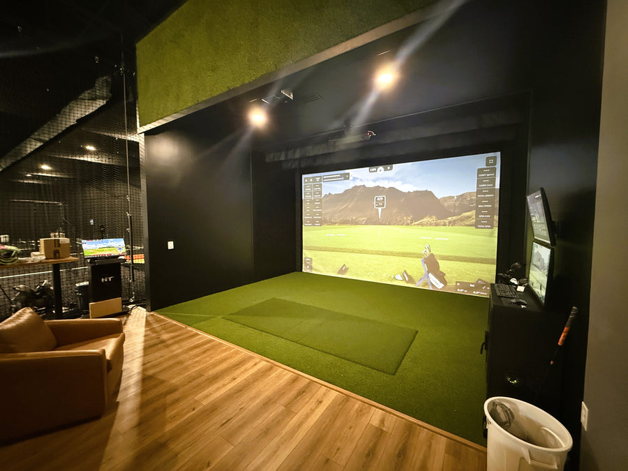 Golf Simulator room built with green turf around it and brown leather seating behind it.