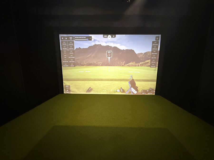 Golf simulator with green turd for hitting area and screen showing a practice round on screen. 