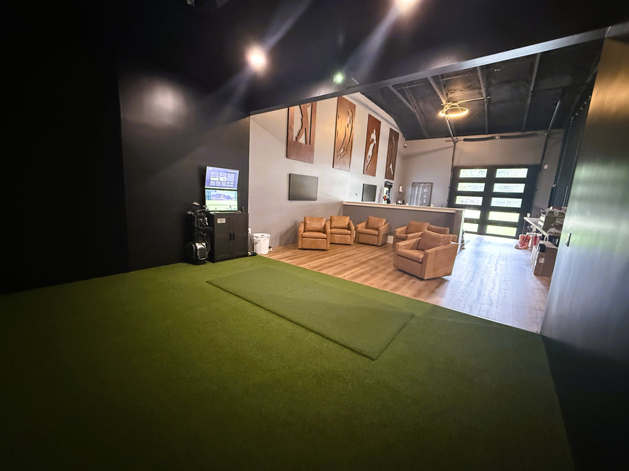 Golf Simulator room built with green turf around it and brown leather seating behind it.