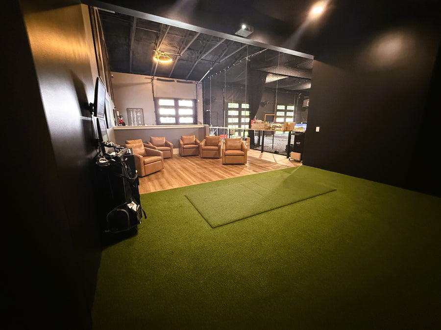 Green turf for golf simulator on the floor with seating in back for gallery to watch.