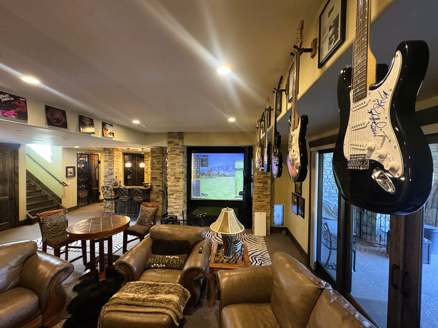 Living room with brown furniture, a guitar on the wall, and an indoor golf simulator.