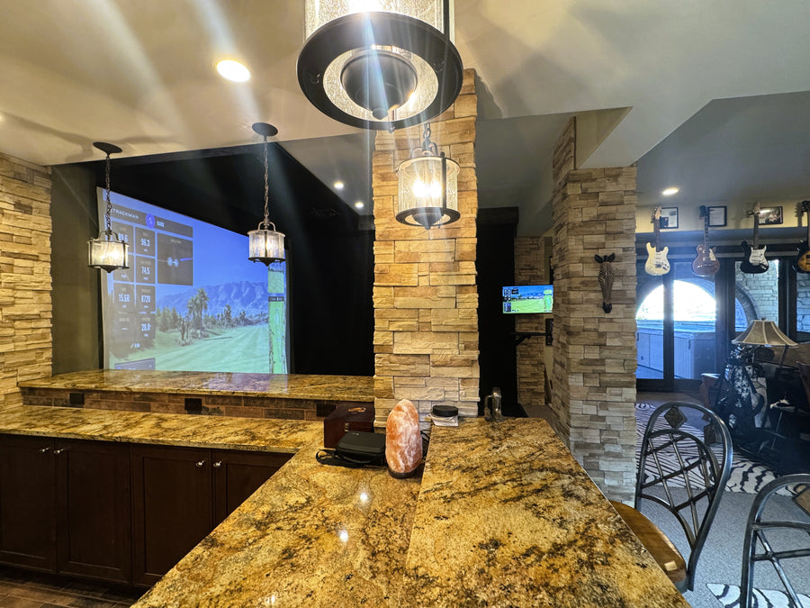 Bar with stone columns, overlooking an indoor golf simulator.