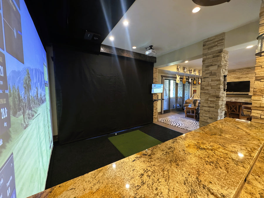 Indoor golf simulator setup in a room with a large screen and projection.
