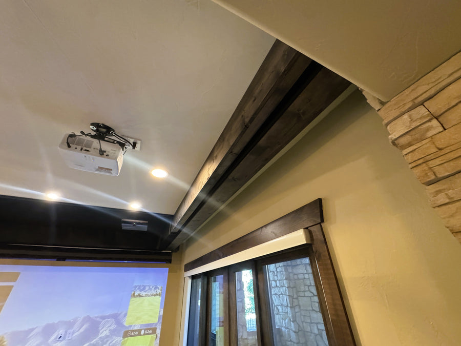 Indoor golf simulator setup with ceiling projector and screen in a room with stone wall.