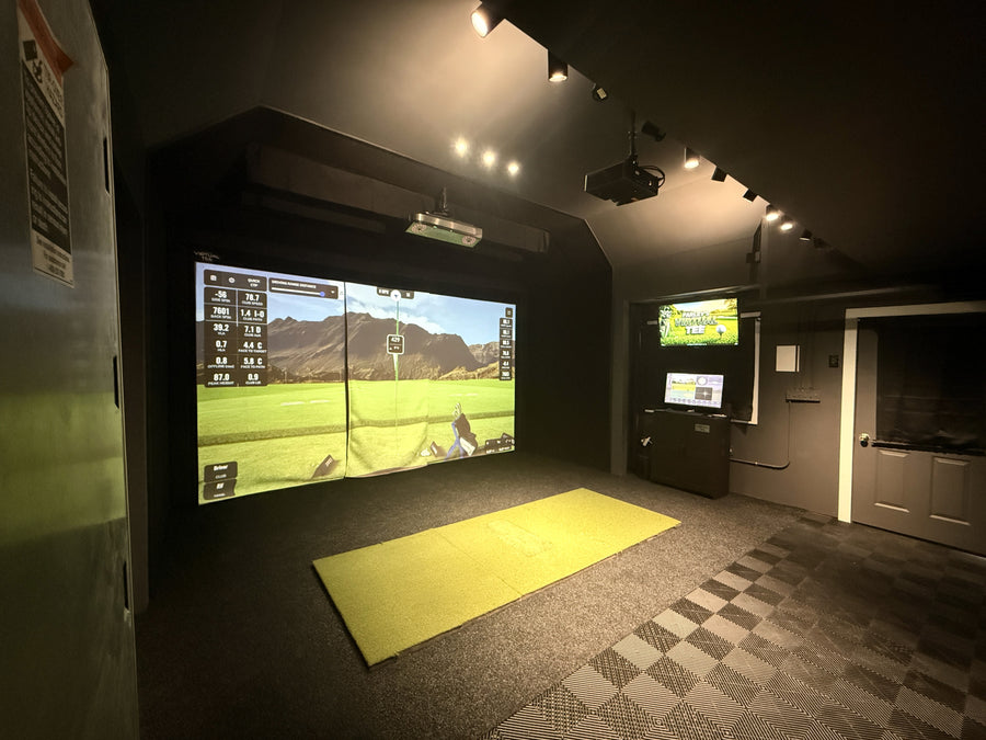 Garage golf simulator with vaulted ceilings and black walls.