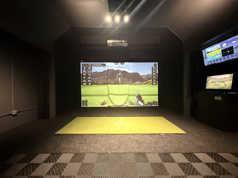 Garage golf simulator with vaulted ceilings and black walls.