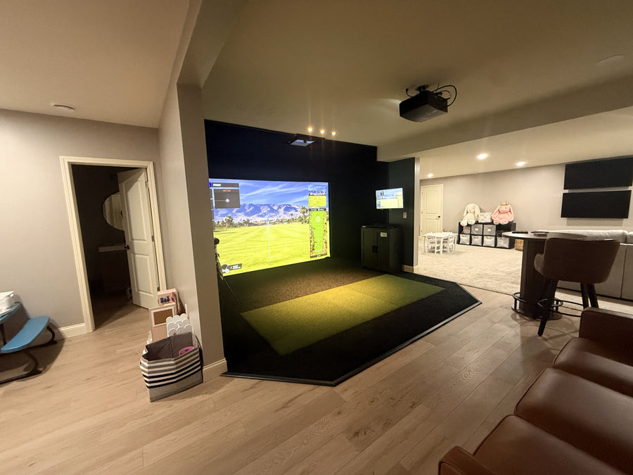 Indoor golf simulator setup in a living room with a large screen displaying a golf course.