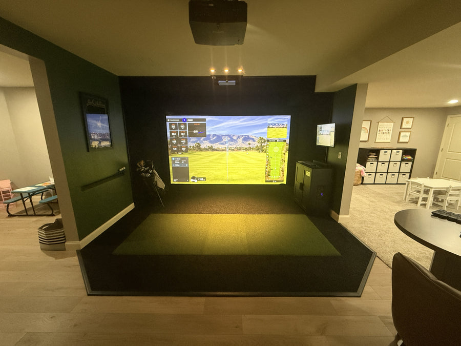 Indoor golf simulator setup in a room with multiple screens and a golf simulator device.