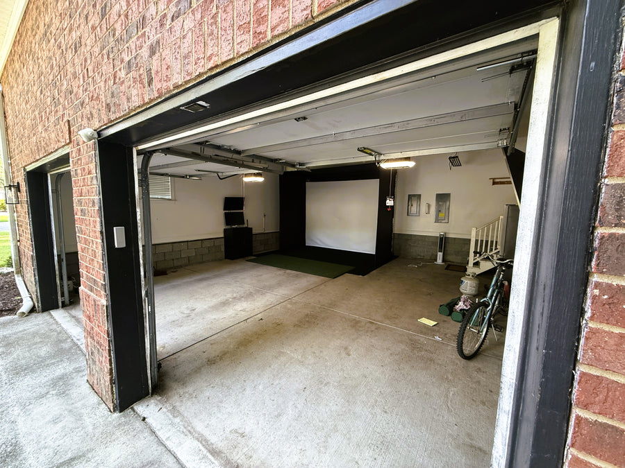 Garage golf simulator with open door showing a projector screen and bicycle.
