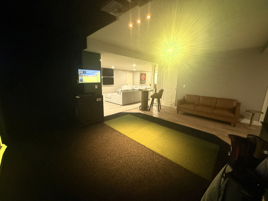 Corner of golf simulator room with couches and lounge area in the back.