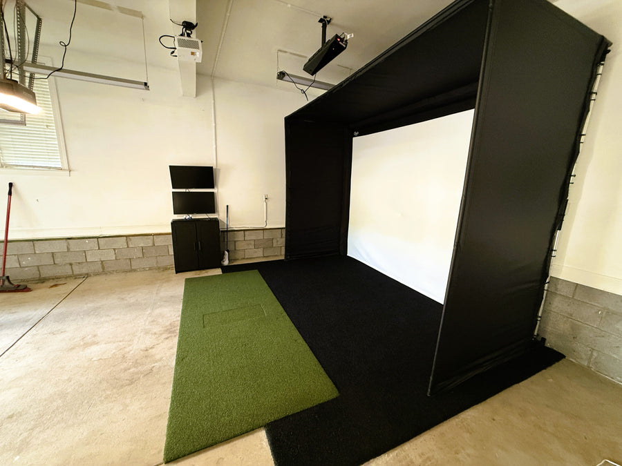 Garage golf simulator setup with green mat and screen.