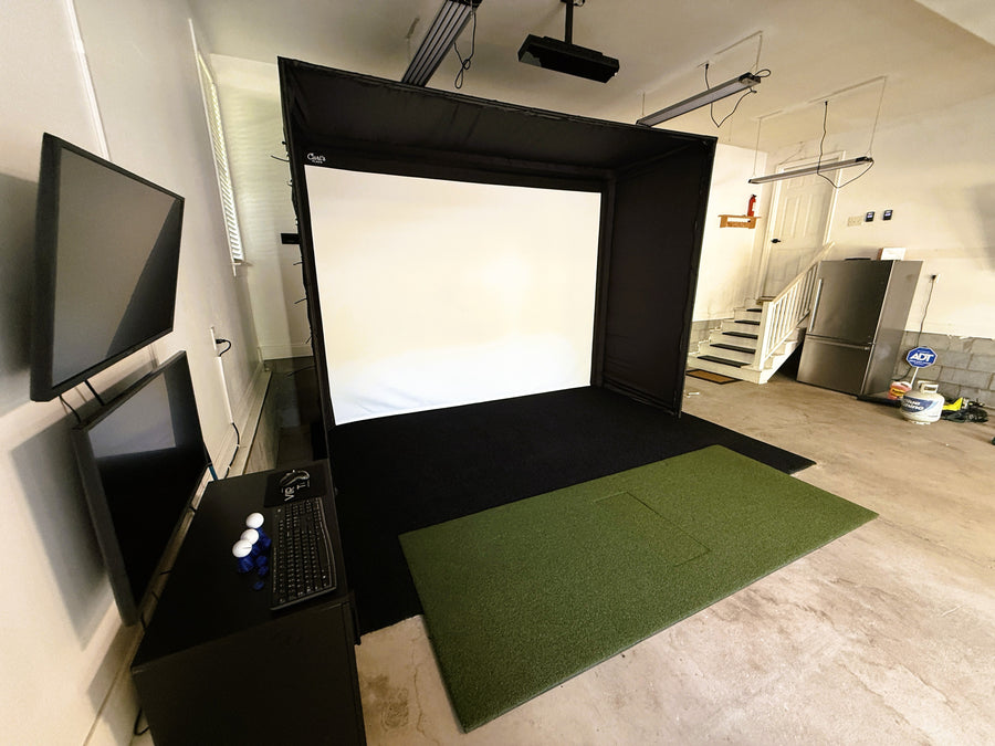 Garage golf simulator setup with screens and a green mat on the floor.