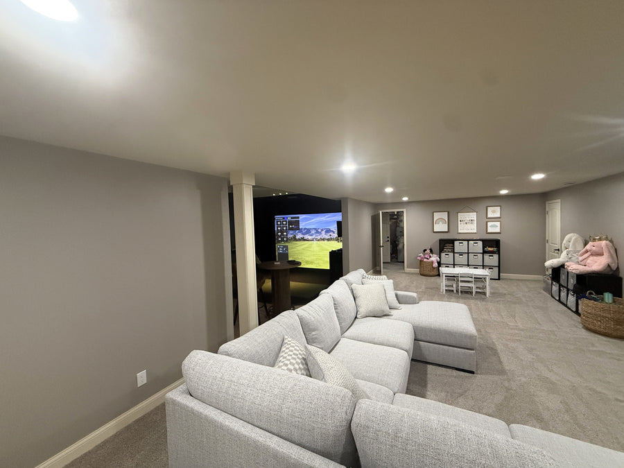 Modern living room with a large sectional sofa and a golf simulator displaying golf round in background.