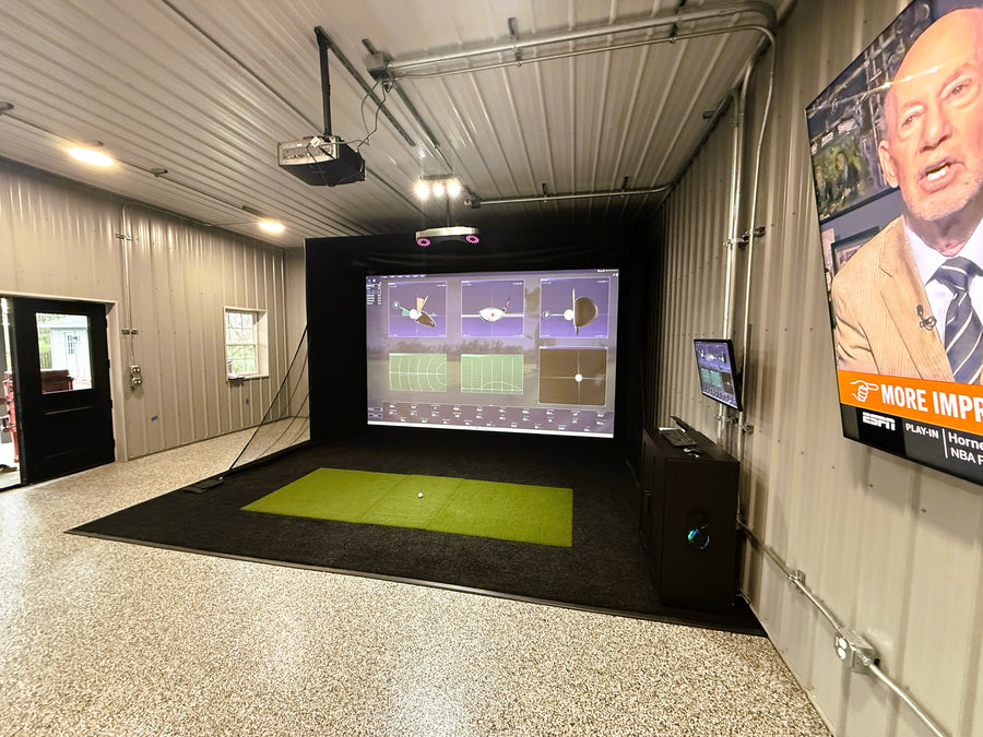Indoor golf simulator setup with screen and green turf in a room.