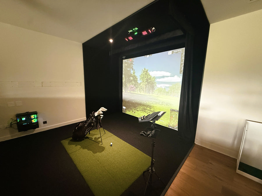 Golf simulator setup with screen, golf club, and ball on a green surface.