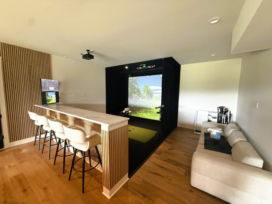 Golf simulator room with a bar area and large screen displaying a golf game.